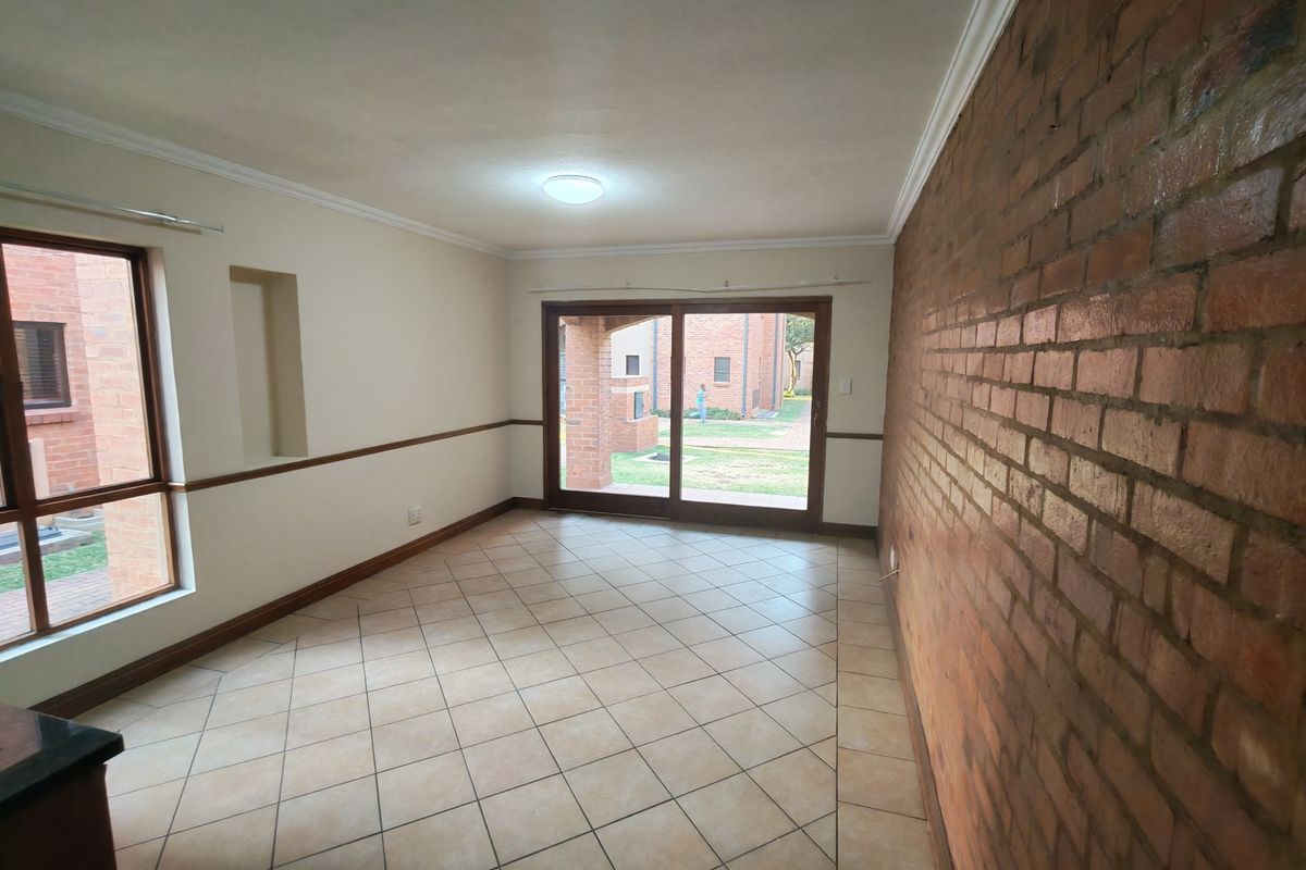 An empty living room featuring an exposed brick feature wall, tiled flooring, and large sliding glass doors providing access to the exterior.
