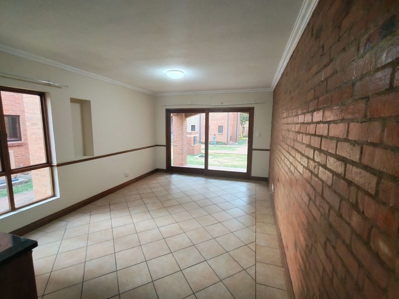 An empty living room featuring an exposed brick feature wall, tiled flooring, and large sliding glass doors providing access to the exterior.
