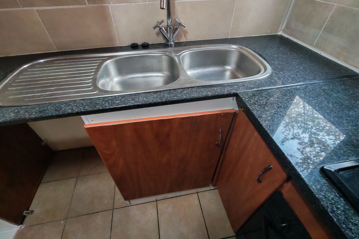 Kitchen area featuring granite countertops, a double stainless steel sink, and tiled backsplash, currently requiring maintenance on the lower cabinetry.