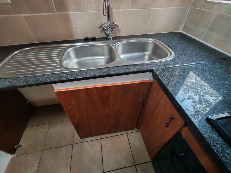Kitchen area featuring granite countertops, a double stainless steel sink, and tiled backsplash, currently requiring maintenance on the lower cabinetry.