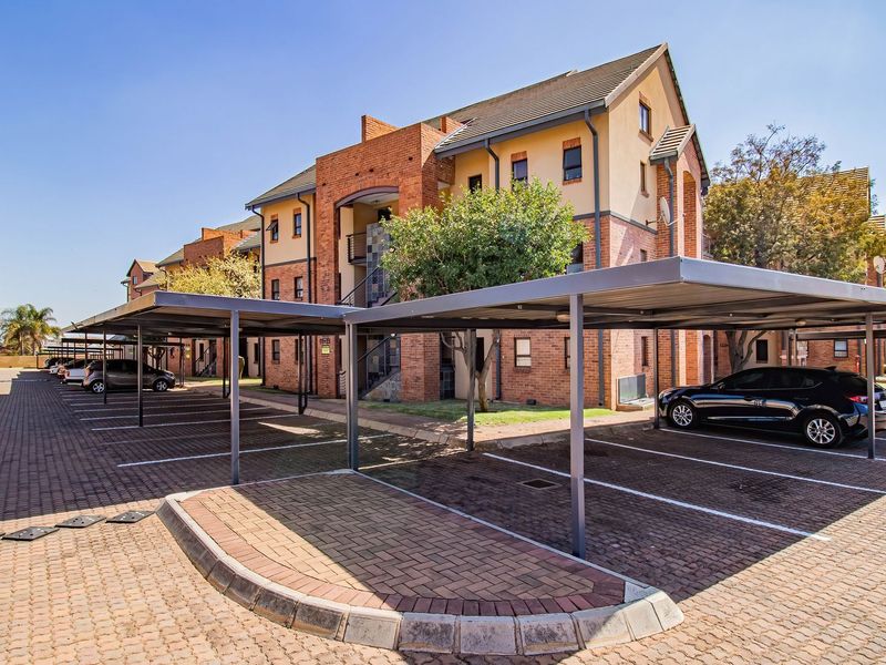 Exterior view of an apartment complex featuring covered parking bays and paved driveway access.