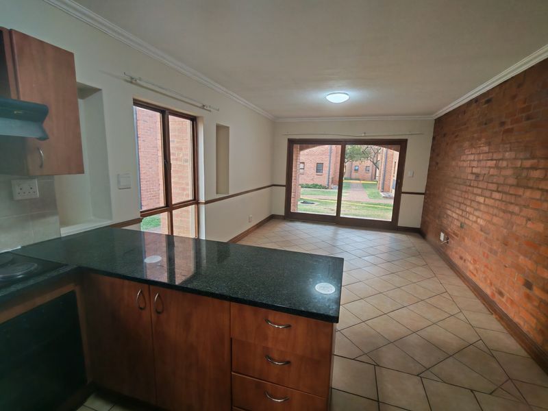 Open-plan kitchen and living area featuring granite countertops, wooden cabinetry, an exposed brick feature wall, and sliding doors leading to the exterior.