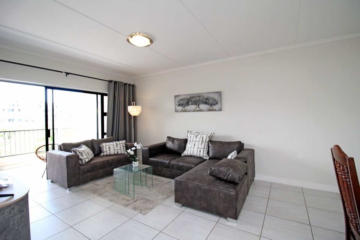A bright living room featuring neutral tiled flooring and a large sliding glass door providing access to an outdoor balcony area.