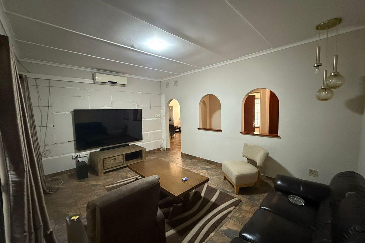 Living room featuring tiled flooring, archway openings, and a wall-mounted air conditioner. The space requires finishing work on the wall paneling.