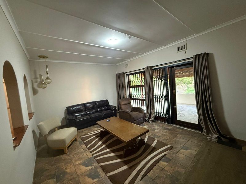A living room featuring tiled flooring, an arched wall detail, and a sliding glass door with security gate leading to an outdoor patio area.