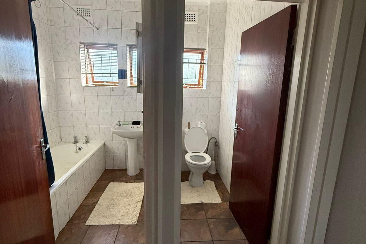 A functional bathroom featuring a pedestal basin, bathtub, and separate toilet area with tiled finishes throughout.