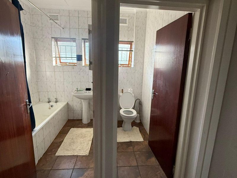 A functional bathroom featuring a pedestal basin, bathtub, and separate toilet area with tiled finishes throughout.