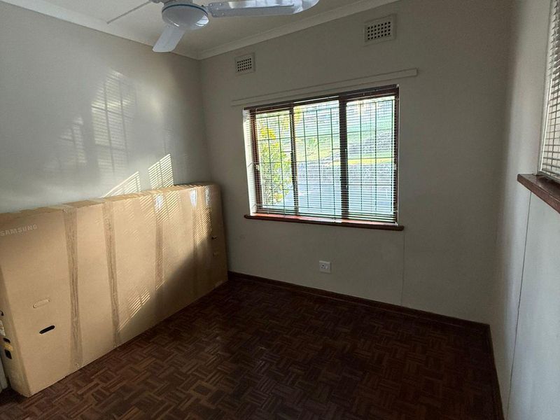 A vacant bedroom featuring classic parquet flooring, a ceiling fan, and venetian blinds, offering a clean and neutral space ready for personalization.