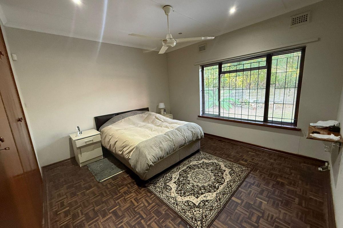 A spacious bedroom featuring classic parquet flooring, a ceiling fan, recessed lighting, and large windows fitted with security bars.