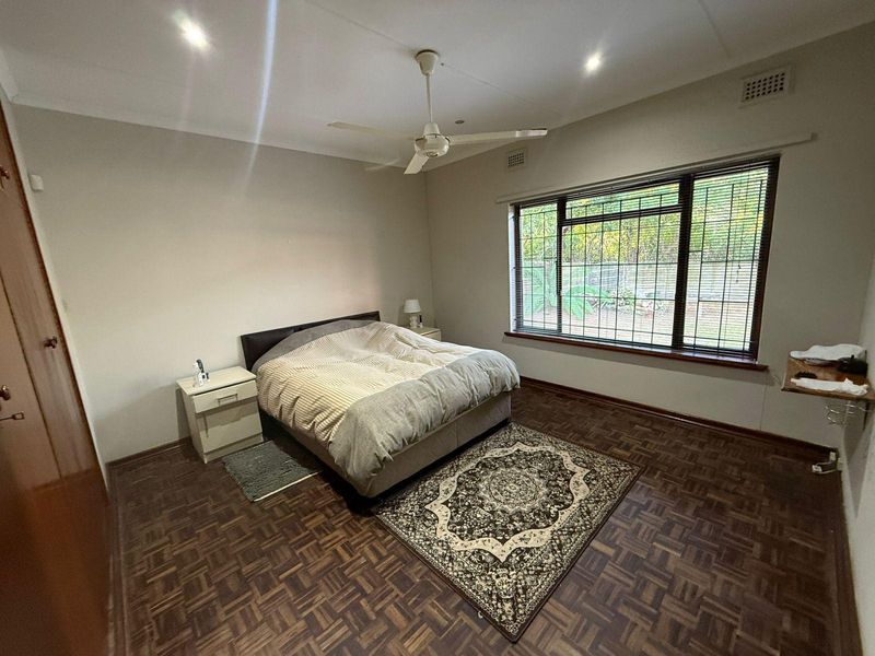 A spacious bedroom featuring classic parquet flooring, a ceiling fan, recessed lighting, and large windows fitted with security bars.