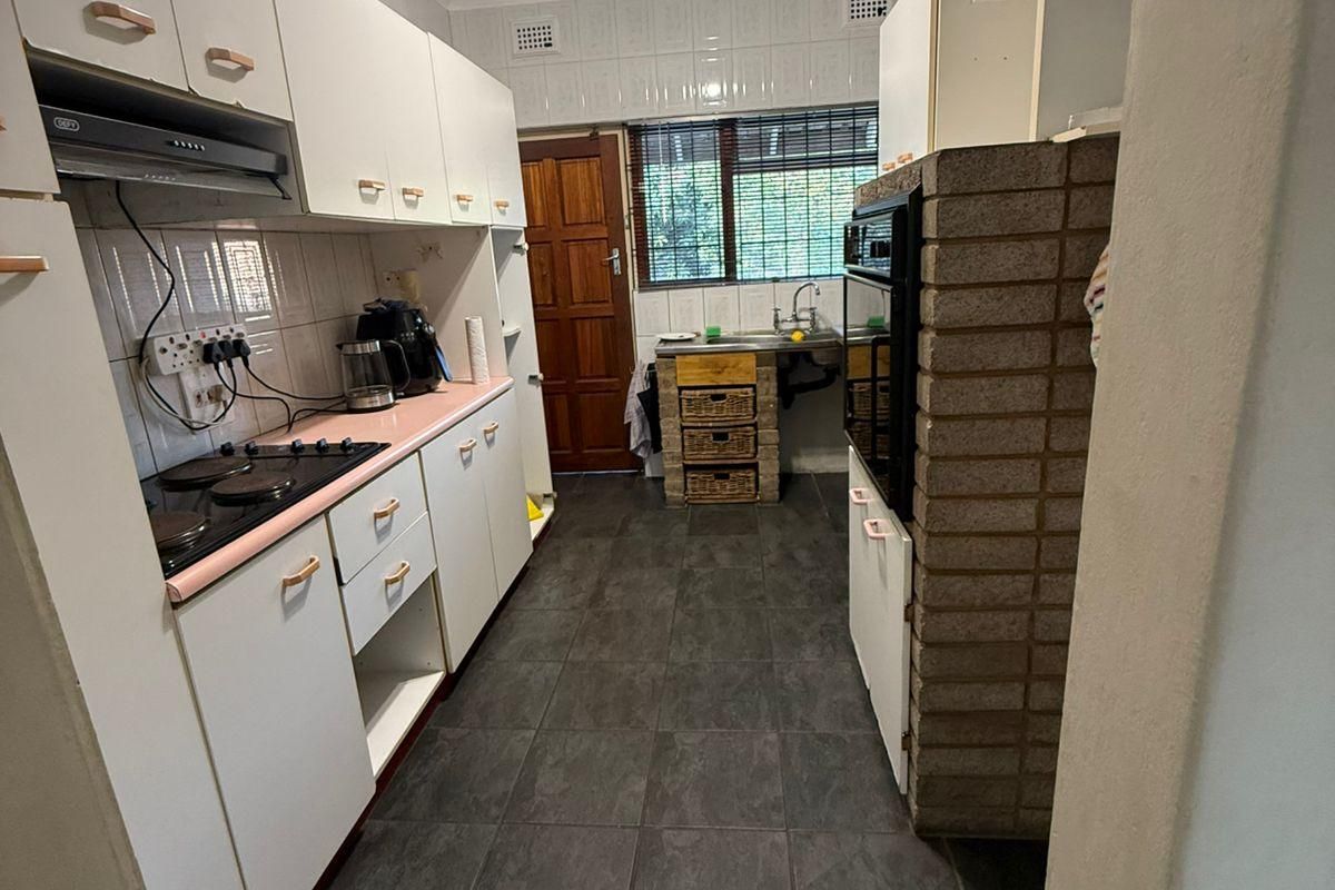 A functional kitchen featuring dark tiled floors, white cabinetry, a built-in oven, and a unique brick feature wall, offering potential for modern renovation.