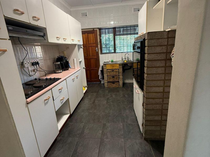 A functional kitchen featuring dark tiled floors, white cabinetry, a built-in oven, and a unique brick feature wall, offering potential for modern renovation.