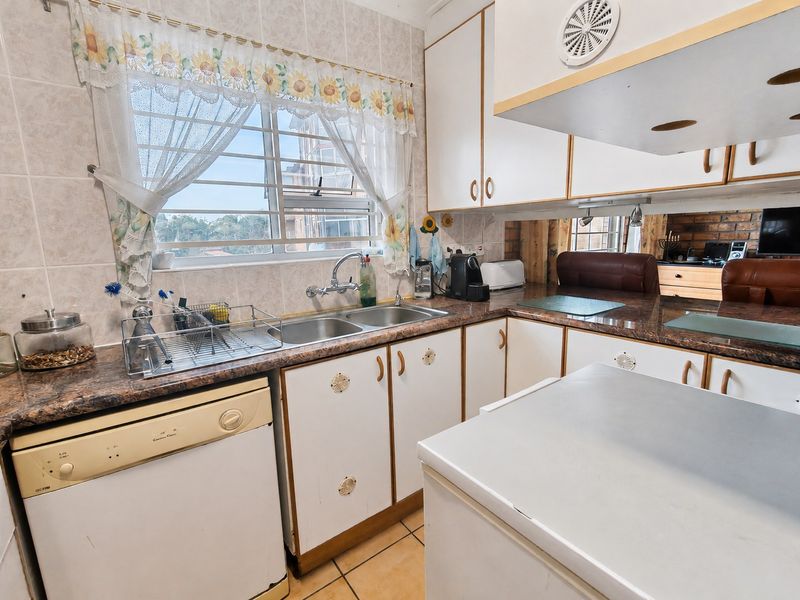 A functional kitchen featuring laminate countertops, double basin sink, tiled backsplash, and ample built-in cabinetry with a window providing natural light.