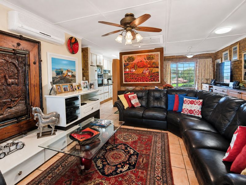 Open-plan living area featuring tiled floors, exposed brick accents, a ceiling fan, and an integrated kitchen with built-in cabinetry and appliances.