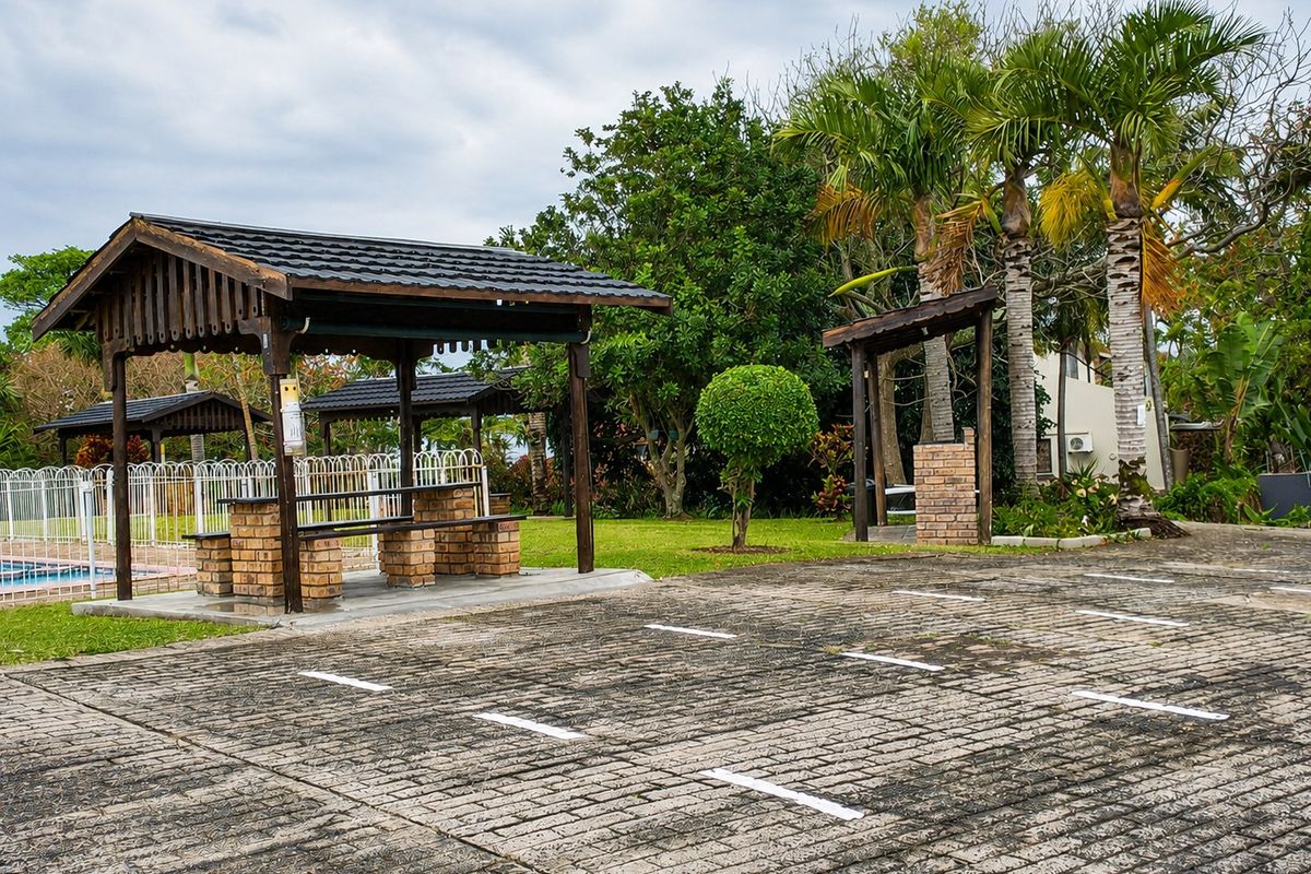 Outdoor communal area featuring a brick-paved parking space, timber gazebo with built-in seating, and landscaped garden surroundings.