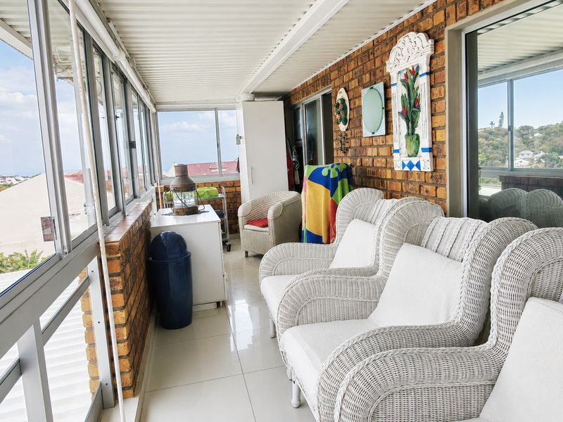 A bright, enclosed balcony featuring exposed brick walls, tiled flooring, and large sliding glass windows offering natural light and outdoor views.