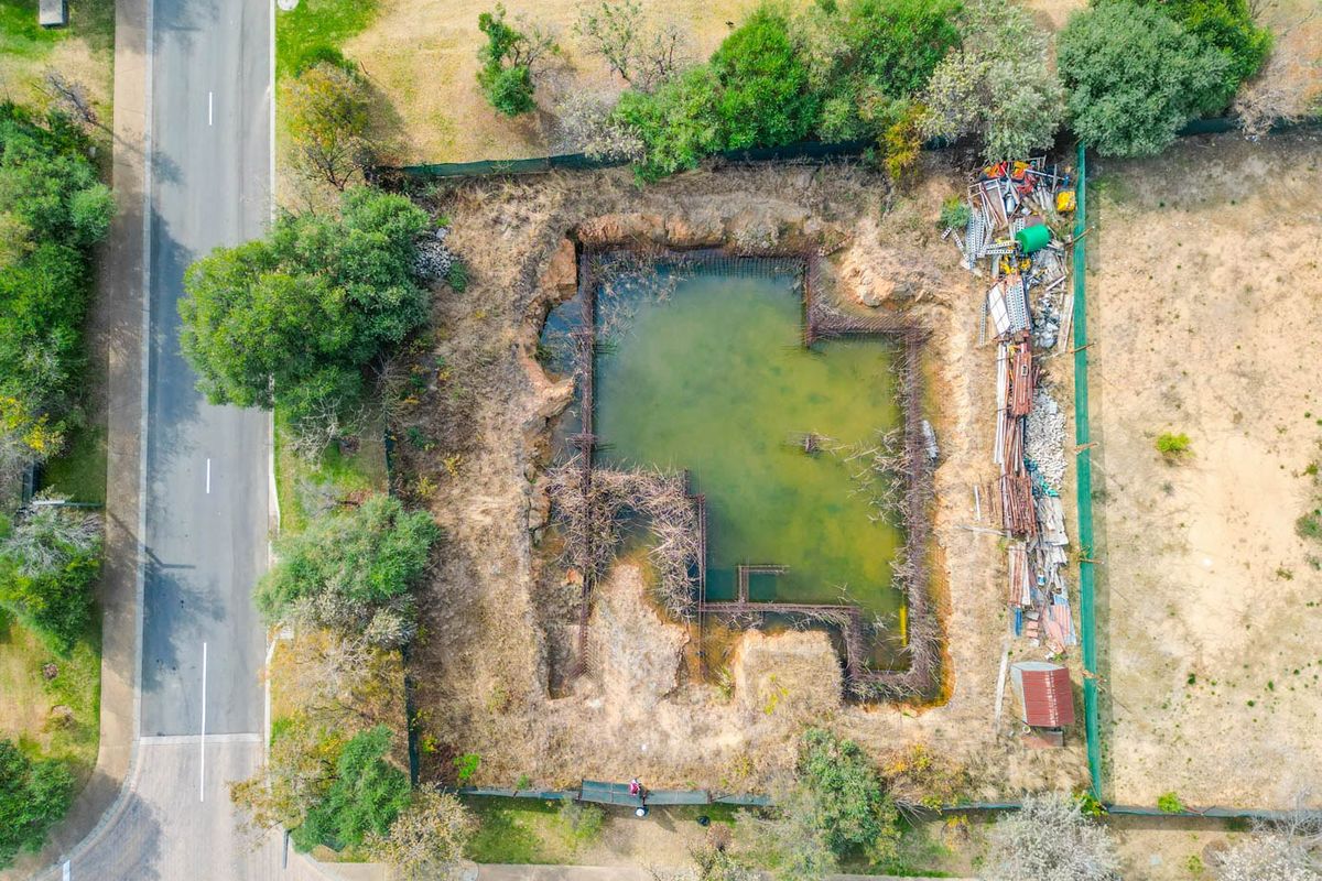 Aerial view of a residential vacant land plot featuring an excavated foundation trench filled with water and exposed steel reinforcement bars.