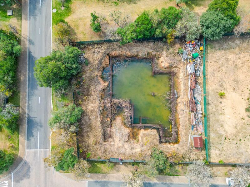 Aerial view of a residential vacant land plot featuring an excavated foundation trench filled with water and exposed steel reinforcement bars.