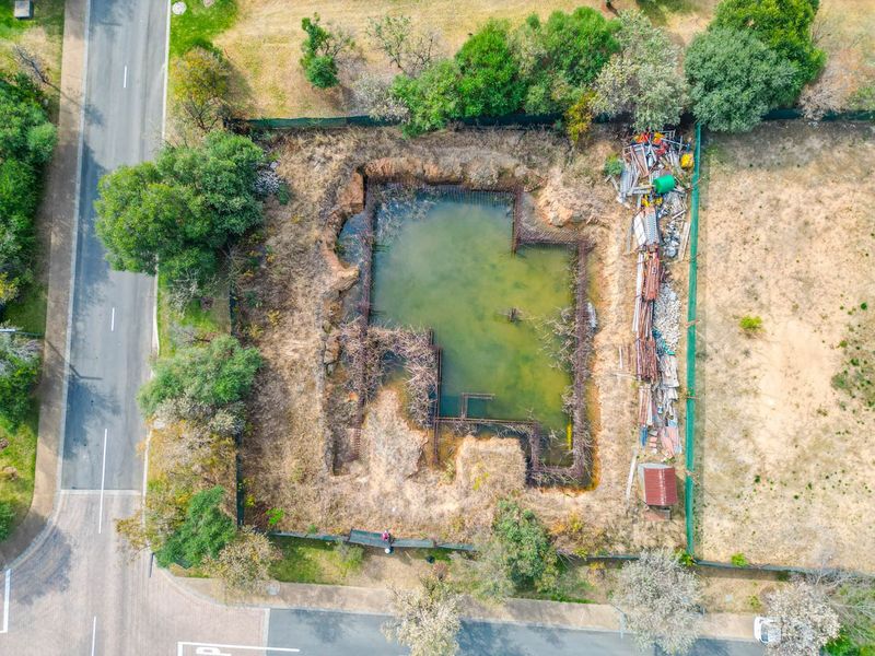 Aerial view of a residential vacant lot featuring an excavated foundation trench with exposed steel reinforcement and stagnant water accumulation.