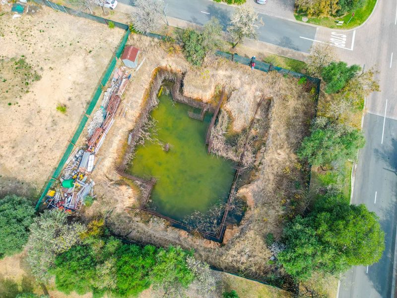 Aerial view of a vacant residential plot featuring an excavated foundation pit with stagnant water and exposed rebar reinforcement.