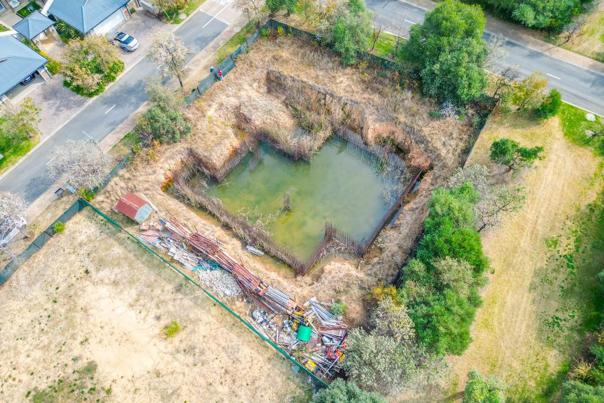 Aerial view of a vacant residential plot featuring a large, flooded excavation pit with exposed steel reinforcement bars and scattered construction debris.