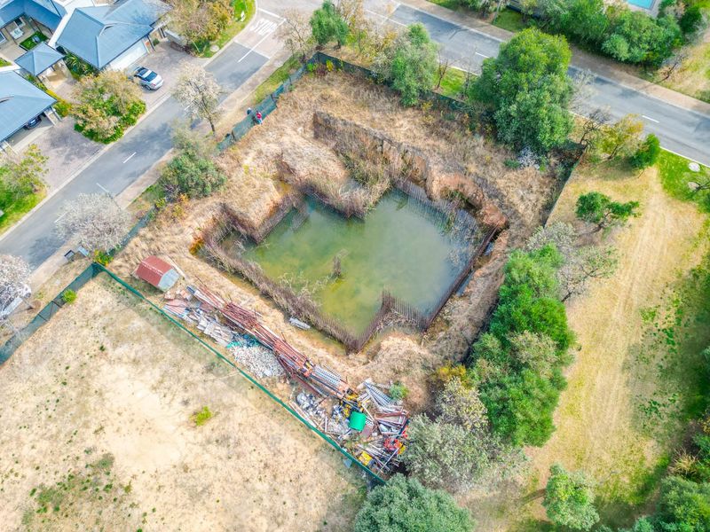 Aerial view of a vacant residential plot featuring a large, flooded excavation pit with exposed steel reinforcement bars and scattered construction debris.