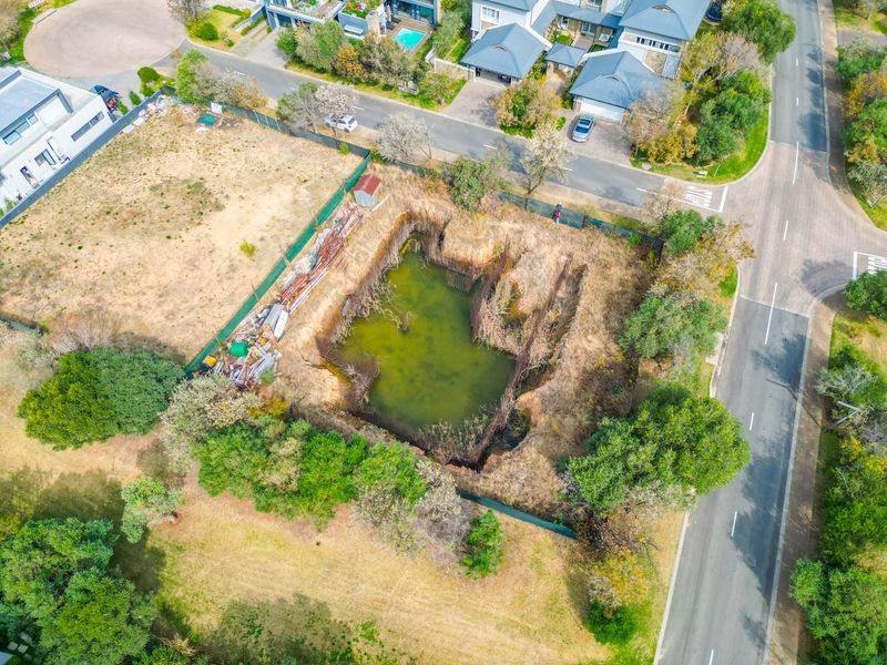 Aerial view of a vacant residential plot featuring an excavated foundation pit with stagnant water and exposed steel reinforcement bars.