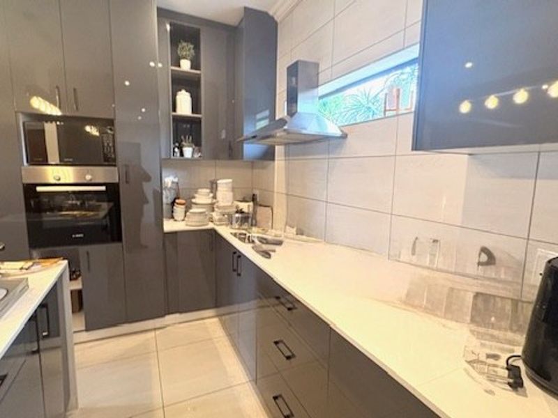 Modern kitchen featuring high-gloss grey cabinetry, stone countertops, integrated oven and microwave, and sleek tiled finishes.