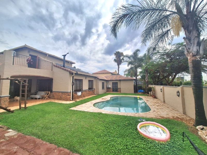 Rear view of the property featuring a swimming pool, covered patio, upper-level balcony, and established garden with perimeter walling.