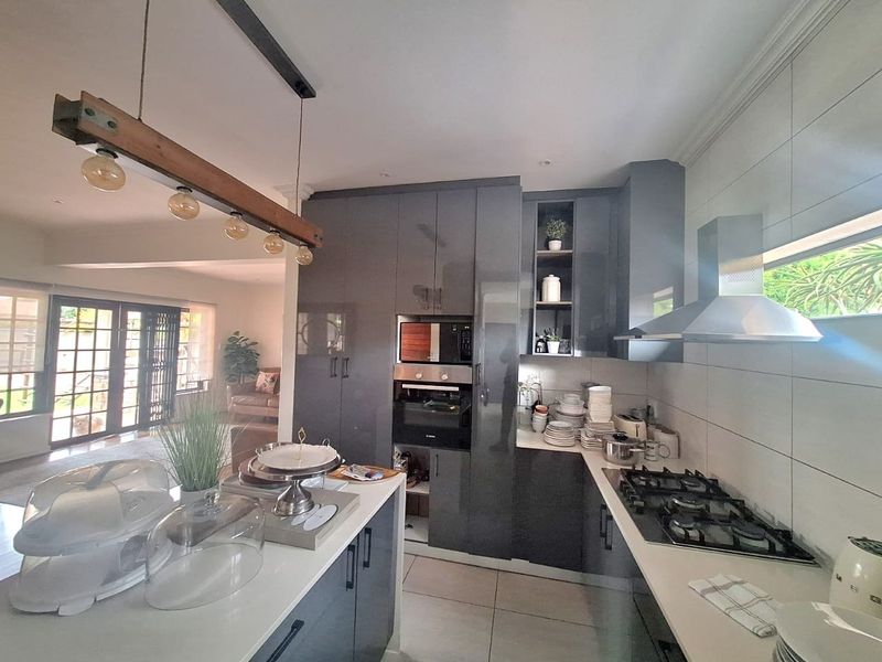 Modern kitchen featuring dark grey cabinetry, a central island, built-in oven and microwave, gas hob with extractor, and tiled flooring, flowing into the living area.
