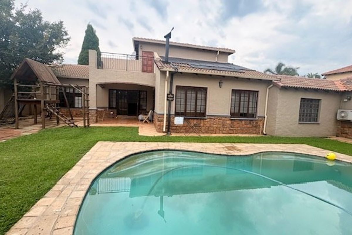 Rear view of the property featuring a swimming pool, paved surround, stone-clad facade, and an upper-level balcony.
