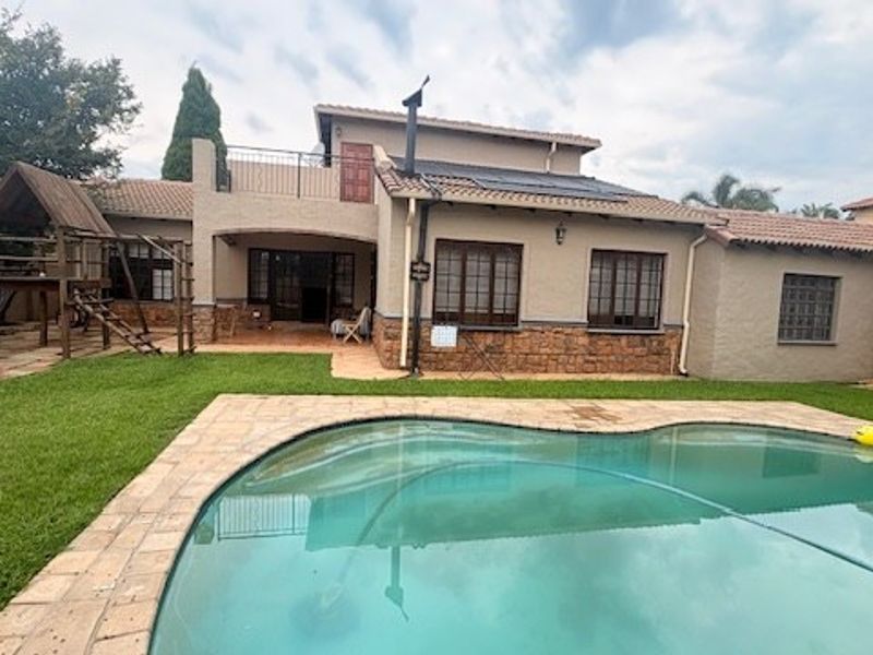 Rear view of the property featuring a swimming pool, paved surround, stone-clad facade, and an upper-level balcony.