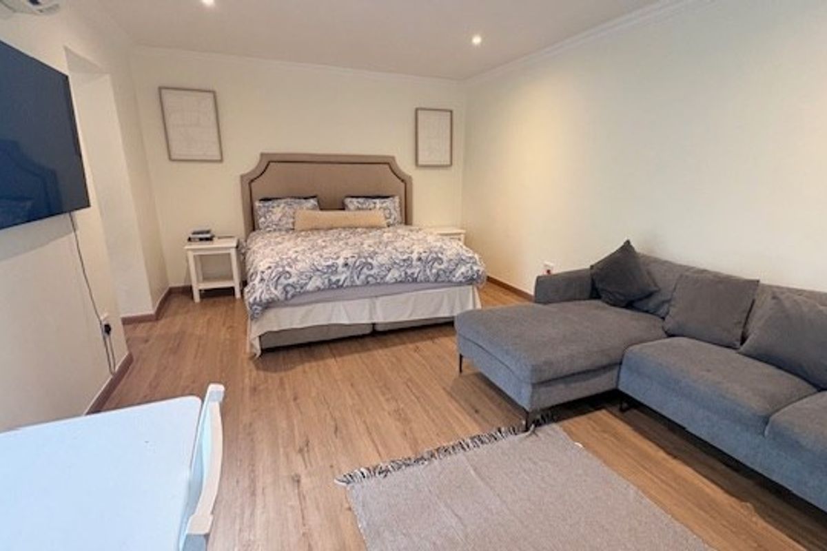 Spacious bedroom featuring light-toned laminate flooring, recessed ceiling lighting, and a wall-mounted air conditioning unit.
