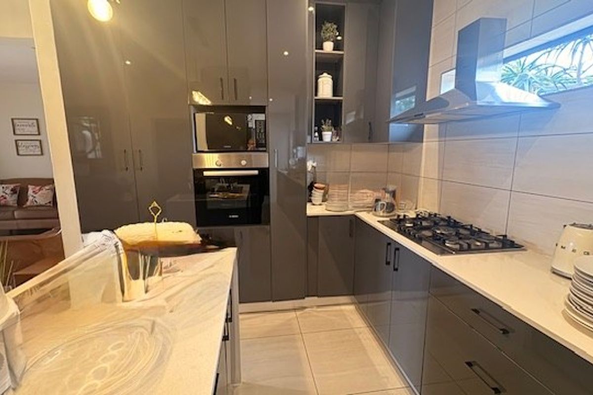 Modern kitchen featuring high-gloss cabinetry, stone countertops, integrated appliances including a gas hob, oven, and microwave, complemented by sleek tiled finishes.