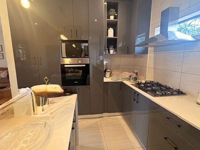 Modern kitchen featuring high-gloss cabinetry, stone countertops, integrated appliances including a gas hob, oven, and microwave, complemented by sleek tiled finishes.