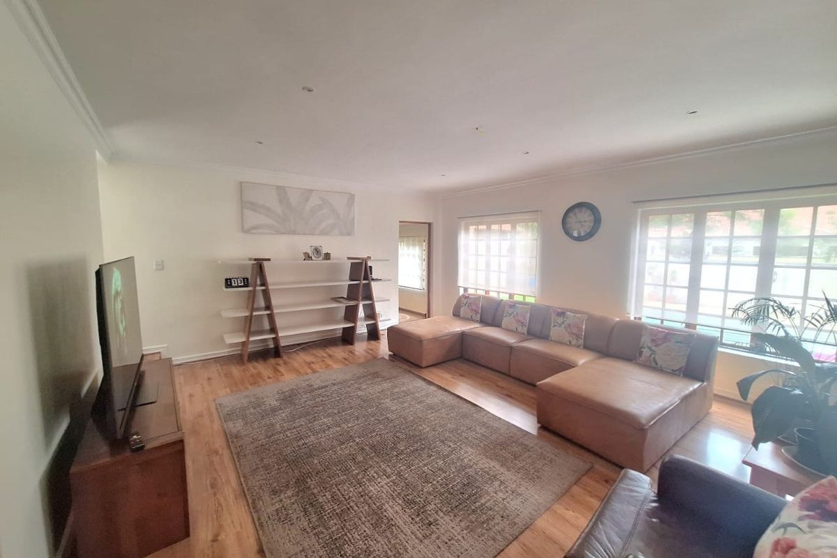 A spacious and bright living room featuring warm timber flooring, recessed downlighting, and large windows that provide ample natural light.