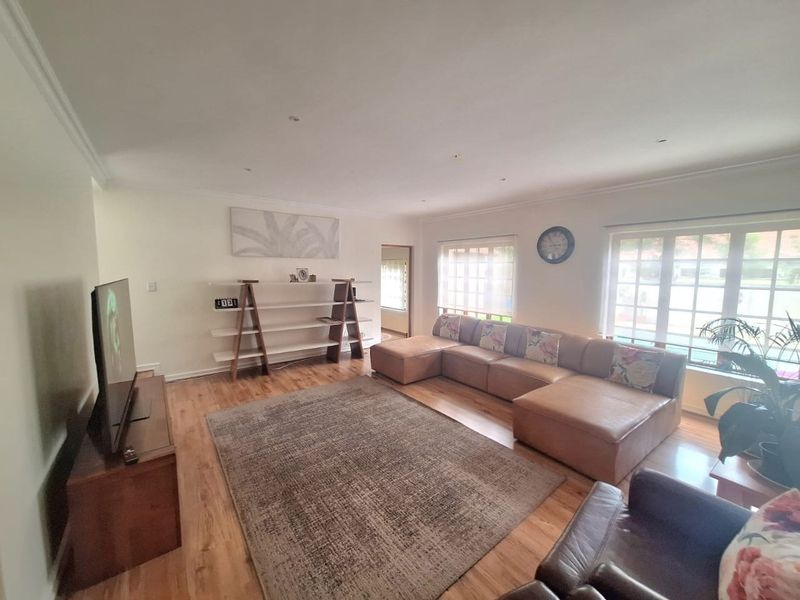 A spacious and bright living room featuring warm timber flooring, recessed downlighting, and large windows that provide ample natural light.