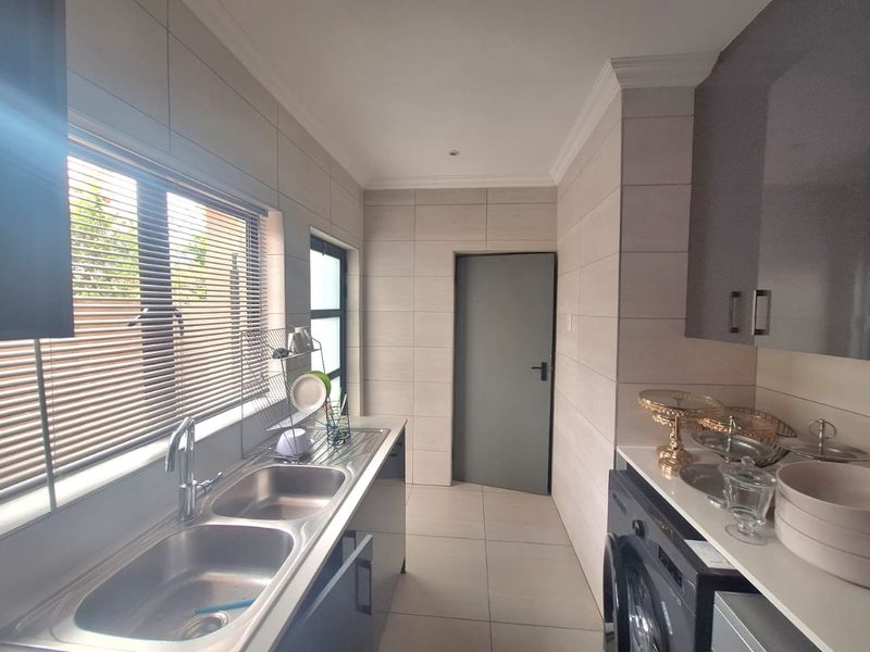 A modern, well-maintained scullery featuring double stainless steel sinks, sleek cabinetry, tiled finishes, and dedicated space for laundry appliances.