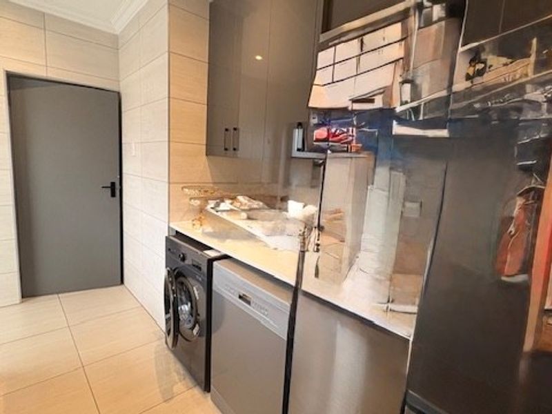 A modern scullery featuring sleek grey cabinetry, stone countertops, tiled finishes, and integrated laundry and dishwashing appliances.