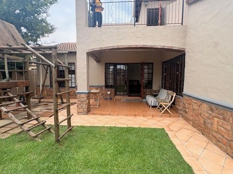 Rear view of the house featuring a covered patio with stone cladding, tiled flooring, and an upper-level balcony with wrought iron railings.