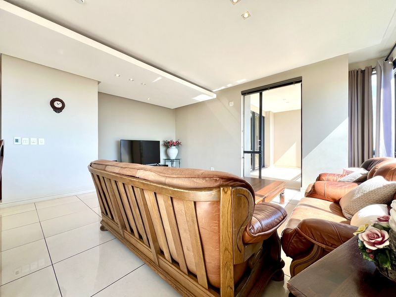 A bright and spacious living room featuring modern tiled flooring, a decorative drop ceiling with recessed lighting, and direct access to an outdoor balcony.