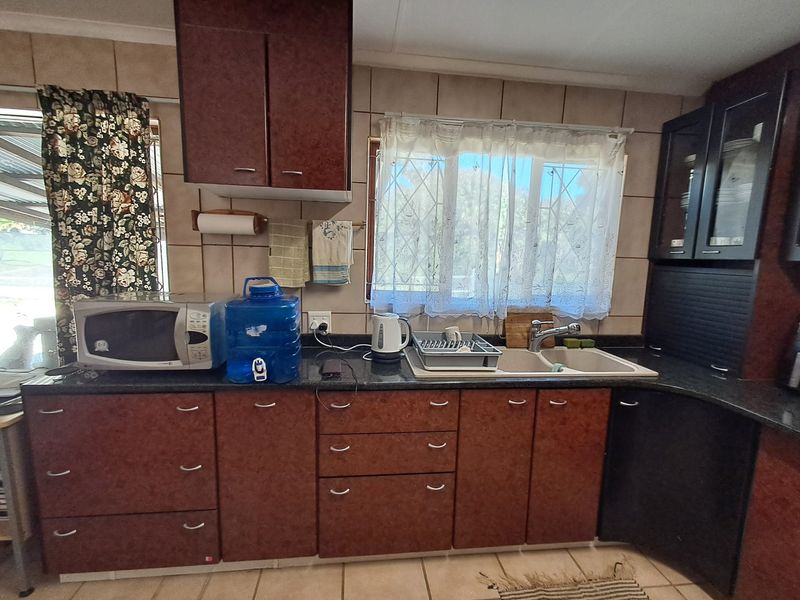 A functional kitchen featuring dark laminate cabinetry, a double basin sink, and tiled backsplash, offering a dated aesthetic ready for modernization.