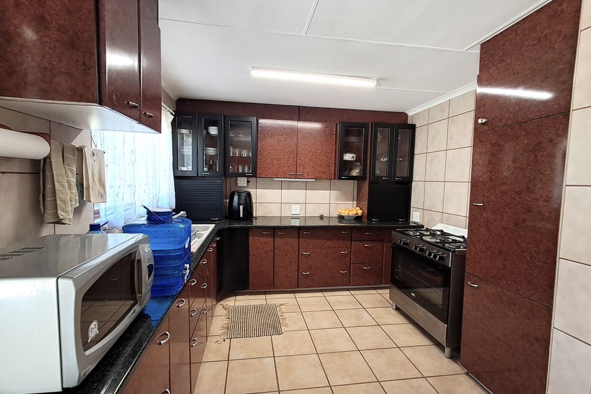 A functional kitchen featuring dark wood-finish cabinetry, granite countertops, tiled flooring, and a freestanding stove with a tiled backsplash.