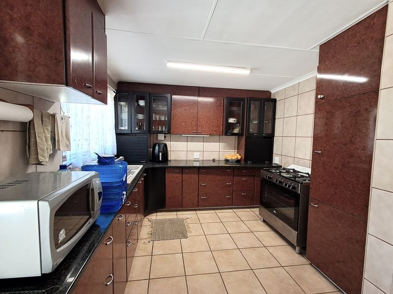 A functional kitchen featuring dark wood-finish cabinetry, granite countertops, tiled flooring, and a freestanding stove with a tiled backsplash.