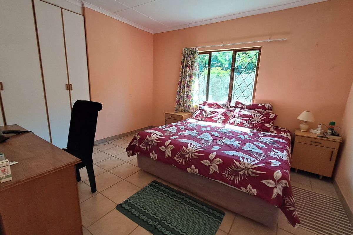 A functional bedroom featuring built-in cupboards, tiled flooring, and a window with security bars, offering a neutral base for potential interior updates.