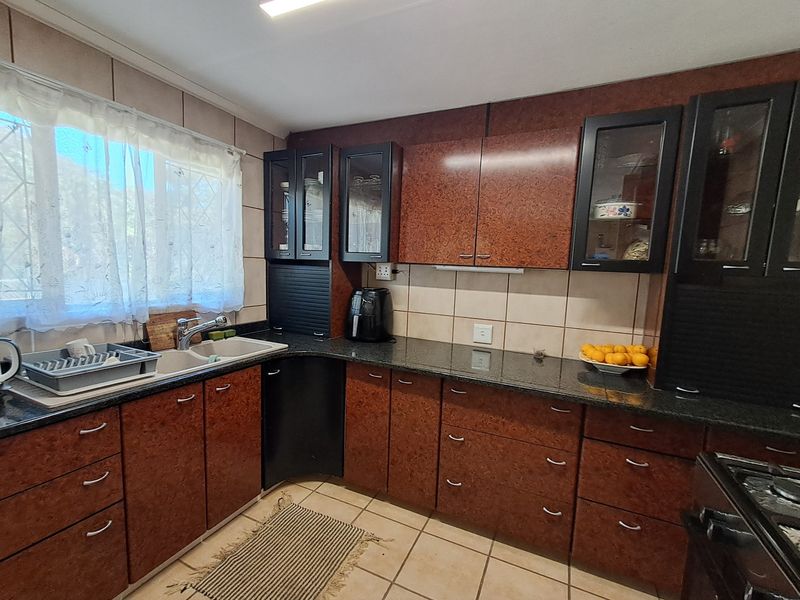 A functional kitchen featuring dark laminate cabinetry, granite countertops, a double basin sink, and tiled flooring with a classic layout.