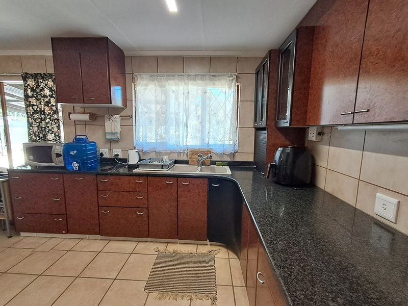 A functional kitchen featuring dark laminate cabinetry, granite countertops, a double basin sink, and tiled flooring with a neutral backsplash.