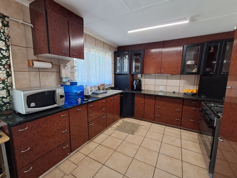 A functional kitchen featuring dark laminate cabinetry, granite countertops, ceramic tile backsplash, and tiled flooring, equipped with a built-in oven and gas hob.