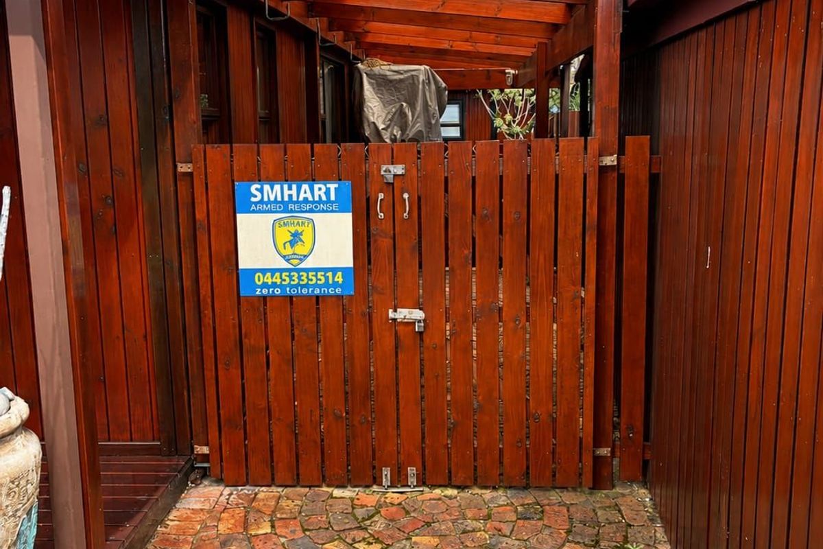 A rear exterior view featuring a timber gate, covered pergola structure, and paved walkway with timber-clad walls.