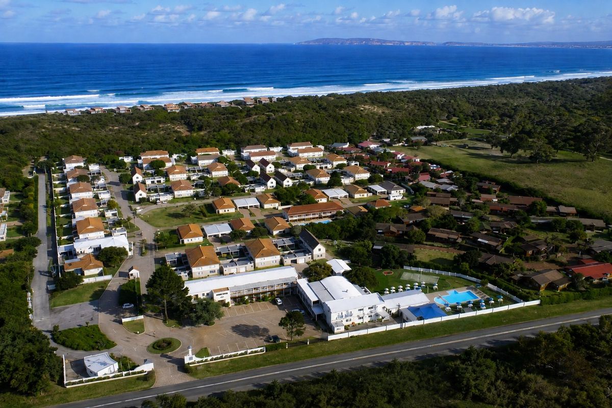 Aerial view of a coastal residential estate featuring multiple dwellings, a swimming pool, tennis court, and proximity to the beach.
